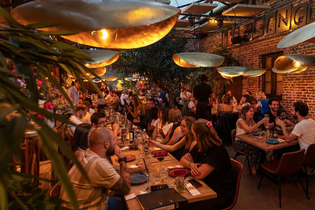 Grande tablée aux Granges : convives réunis sous les lampes en laiton, le long du mur de briques.