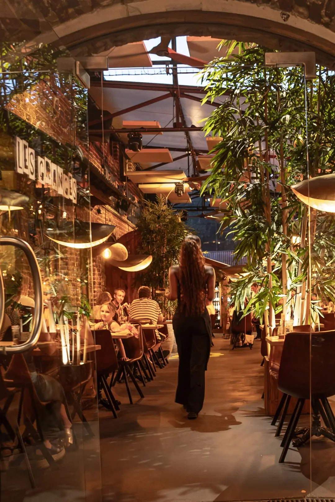 La terrasse couverte des Granges, tables dressées entre les bambous sous les lampes en laiton.